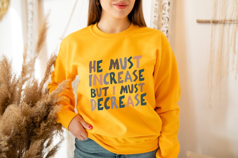 K&ouml;nnte beinhalten: Gelber Pullover mit dem Text "He must increase but I must decrease" in bunten Buchstaben.