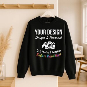 May include: Black sweatshirt with white text: "YOUR DESIGN Unique & Personal" and a camera icon. Below, text reads "Text, Photos & Graphics Endless Possibilities!" in various colours. The sweatshirt is hanging on a white hanger.