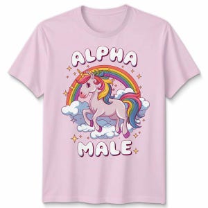 May include: Pale pink t-shirt with a cartoon unicorn design. The unicorn has a rainbow mane and tail, and stands on clouds in front of a rainbow. The words "ALPHA MALE" are printed above and below the unicorn.