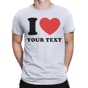 Puede incluir: Camiseta blanca con una "I" negra y un coraz&oacute;n rojo. El texto "YOUR TEXT" est&aacute; impreso debajo del coraz&oacute;n.
