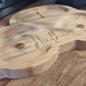 May include: A light brown wooden serving tray with three small bowls and the name "Haitham" engraved on the surface.