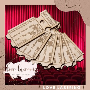 May include: A set of six wooden movie ticket stubs with the text "ADMITS ONE" and "Beauty & The Beast" printed on them. The tickets are arranged in a fan shape and are set against a red velvet curtain backdrop.