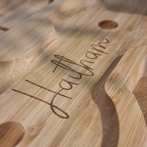 May include: A close-up of a wooden serving tray with the word "Hallmark" engraved on the surface. The tray has a natural wood finish and is designed to hold multiple items.