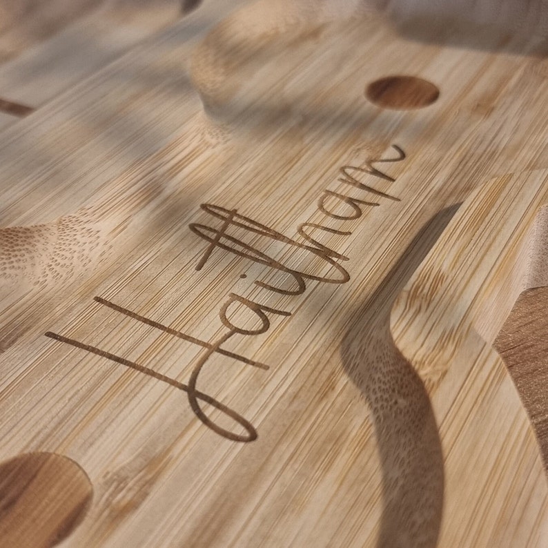 May include: A close-up of a wooden serving tray with the word "Hallmark" engraved on the surface. The tray has a natural wood finish and is designed to hold multiple items.