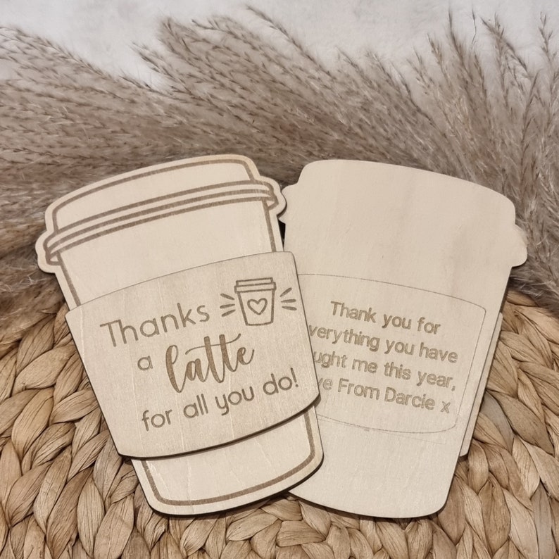 May include: A wooden coffee cup sleeve with the text "Thanks a latte for all you do!" and a small heart. The sleeve is attached to a separate wooden coffee cup cutout with the text "Thank you for everything you have taught me this year, Love From Darcie x".