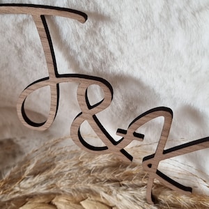 May include: Wooden cutout of the letters "J & A" in a cursive font. The letters are painted black and are on a light brown background.