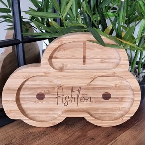 May include: A wooden car-shaped serving tray with two compartments. The tray is made of natural bamboo and has the name "Ashton" engraved on the front.