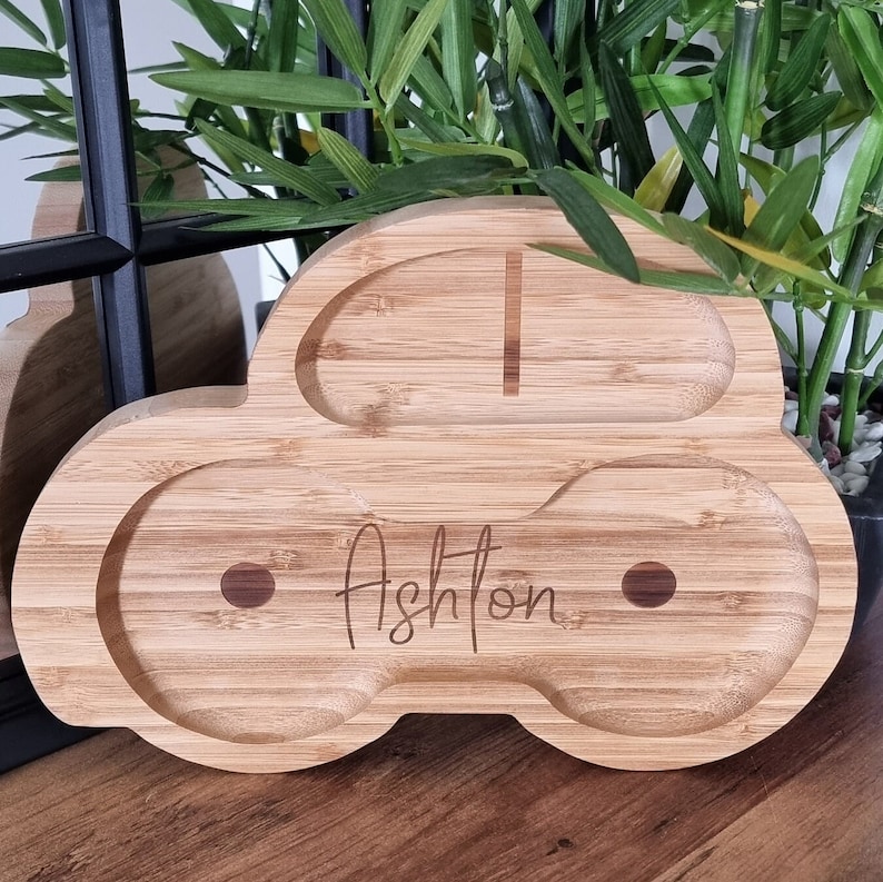 May include: A wooden car-shaped serving tray with two compartments. The tray is made of natural bamboo and has the name "Ashton" engraved on the front.