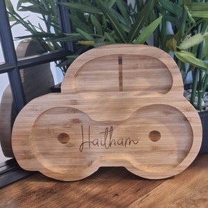 May include: A wooden car-shaped serving tray with two compartments and a small handle. The tray is engraved with the name "Haitham".