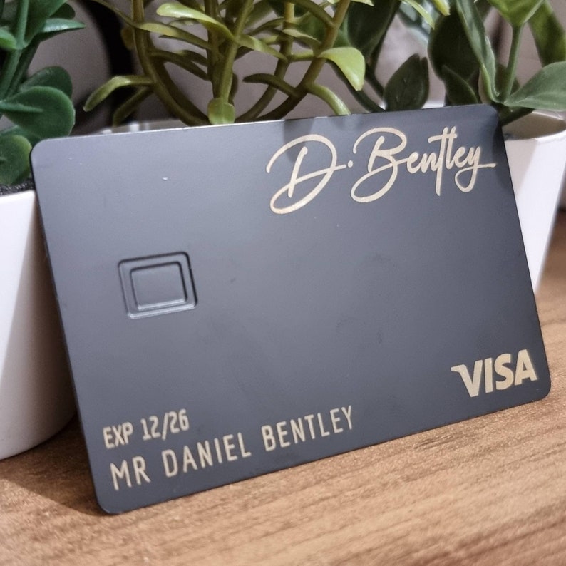 Pu&ograve; includere: Una carta di credito nera con lettere dorate. La carta ha il nome "D. Bentley" e il testo "EXP 12/26 MR DANIEL BENTLEY" sul davanti. Il logo VISA &egrave; in basso a destra.
