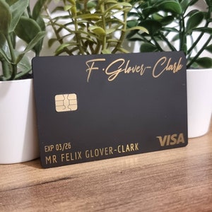 Pu&ograve; includere: Carta di credito nera con scritte dorate. La carta ha il nome "F. Glover-Clark" e il testo "EXP 03/26 MR FELIX GLOVER-CLARK" e il logo VISA.