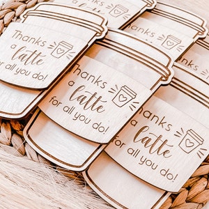 May include: Set of six wooden coffee cup shaped tags with the text "Thanks a latte for all you do!" and a small coffee cup icon. The tags are light brown and have a natural wood grain.
