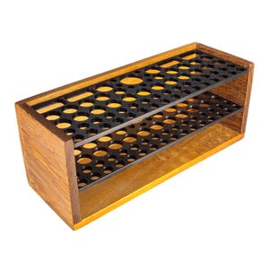 May include: A wooden test tube rack with two black perforated shelves. The rack is made of light brown wood with a rectangular shape and is designed to hold multiple test tubes. The background is white.