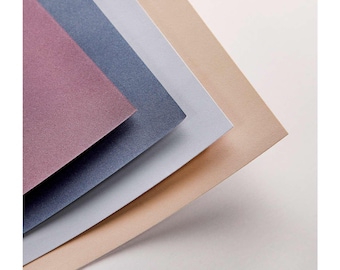 Könnte beinhalten: Ein Stapel strukturierter Papierbögen in den Farbtönen Mauve, Marineblau, Hellgrau und Beige. Die Papiere sind diagonal angeordnet und zeigen ihre unterschiedlichen Farben und den subtilen Glanz. Der Hintergrund ist schlicht weiß.