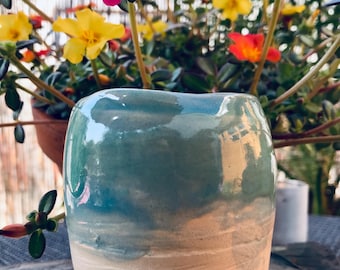 May include: A small, handmade ceramic vase with a light blue and white glaze. The vase has a rounded shape and a slightly uneven rim.