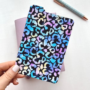 May include: A rectangular planner divider featuring a vibrant leopard print pattern in shades of blue, purple, and yellow against a black background. The divider has rounded corners and a single tab at the top edge for organization in a binder.