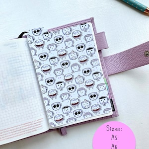 May include: A lavender planner with a coffee cup pattern cover, open to a lined page. A teal pen with a gold tip rests nearby. A pink circle lists planner sizes: A5, A6, and B6.
