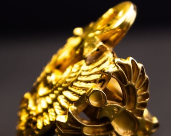 May include: A gold ring featuring a detailed design of two birds with outstretched wings.