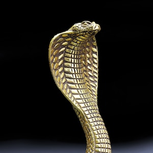 May include: A golden cobra statue with a detailed, textured surface. The snake is in a striking, upright pose, with its hood flared. The sculpture is set against a dark background, highlighting the intricate design and golden color.
