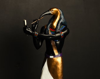 Könnte beinhalten: Eine schwarze und goldene Statue des ägyptischen Gottes Thoth, dargestellt als Mann mit dem Kopf eines Ibis. Er hält einen Stab in seiner rechten Hand und eine Schriftrolle in seiner linken Hand. Die Statue steht auf einem schwarzen Sockel mit Hieroglyphen.