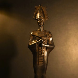 May include: A black metal statue of an Egyptian pharaoh with a tall, ornate headdress. The statue is standing on a square base with intricate carvings.