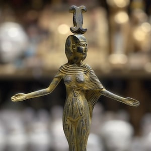 May include: A gold-colored statue of an Egyptian goddess with a headdress. The statue is standing on a square base.