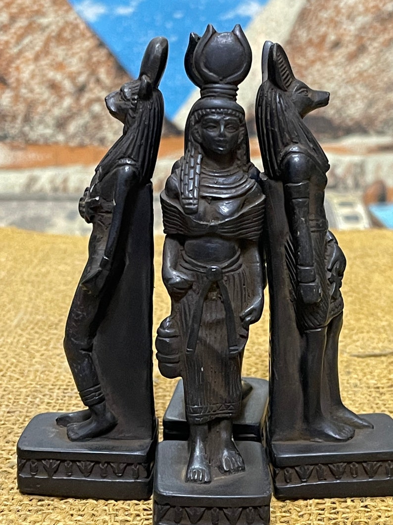 May include: Three black figurines of Egyptian deities. The center figure is a woman with a tall headdress, the figure on the left is a jackal-headed god, and the figure on the right is a dog-headed god.