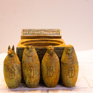May include: Four small, green, carved stone figures of Egyptian gods, each with a different design, sitting in front of a small, green, carved stone box with hieroglyphics.