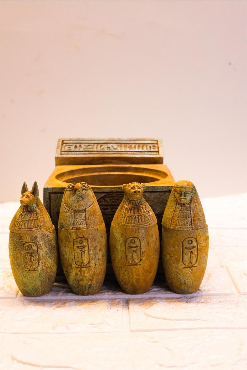 May include: Four small, green, carved stone figures of Egyptian gods, each with a different design, sitting in front of a small, green, carved stone box with hieroglyphics.
