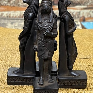 May include: Three black statues of Egyptian deities. The statues are standing on small square bases. The statue on the left is a jackal-headed god, the middle statue is a falcon-headed god, and the statue on the right is a rabbit-headed god.