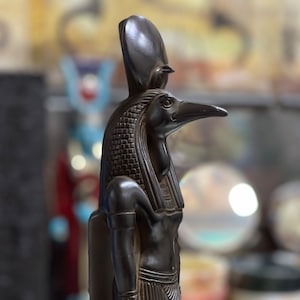 May include: Black statue of the Egyptian god Anubis, depicted as a jackal with a human body. The statue is wearing a headdress and has a detailed design.