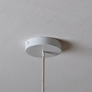 Puede incluir: Un dosel de techo blanco con un dise&ntilde;o circular, con un tornillo visible y un cable beige que se extiende hacia abajo. El dosel est&aacute; montado en un techo blanco texturizado, lo que sugiere una instalaci&oacute;n de iluminaci&oacute;n.
