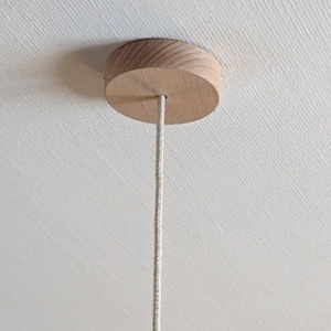 Puede incluir: Un dosel de techo de madera clara, de dise&ntilde;o redondo. Un cable beige se extiende desde el centro del dosel, colgando hacia abajo. El dosel est&aacute; montado en un techo blanco.