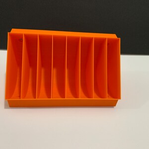 K&ouml;nnte beinhalten: Orangefarbener Plastik-Organizer mit acht F&auml;chern. Der Organizer ist f&uuml;r die Aufbewahrung von kleinen Gegenst&auml;nden wie Stiften, Bleistiften oder Bastelbedarf konzipiert.