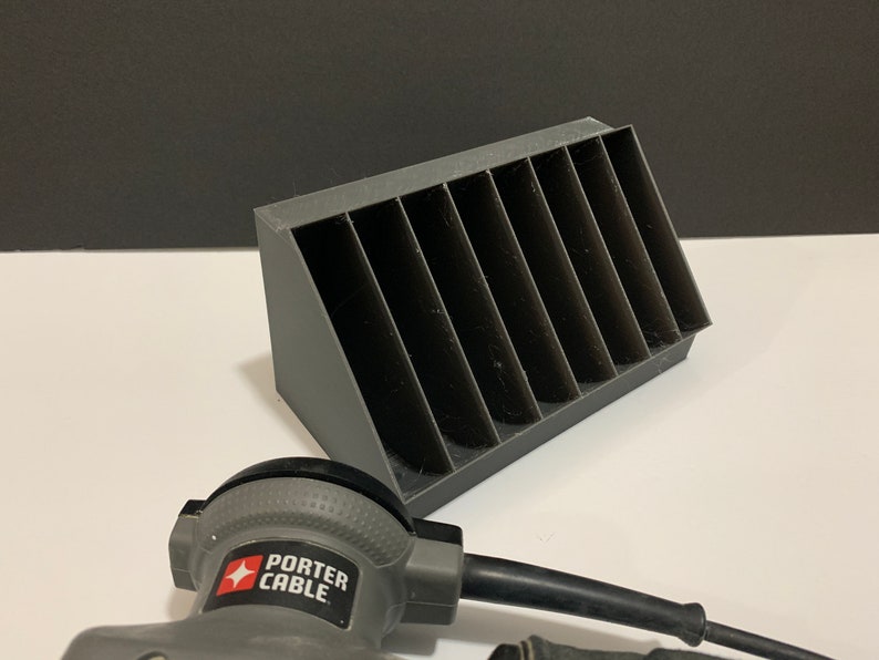 K&ouml;nnte beinhalten: Ein grauer Plastik-Organizer mit acht F&auml;chern zur Aufbewahrung von Kleinteilen. Der Organizer ist abgewinkelt und hat eine strukturierte Oberfl&auml;che. Ein graues Elektrowerkzeug mit dem Text "PORTER CABLE" befindet sich im Vordergrund.