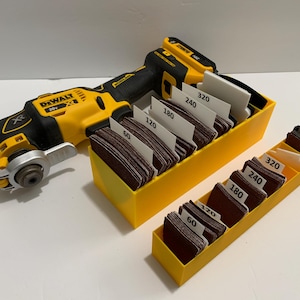 May include: A yellow and black DeWalt oscillating tool with a sanding attachment. The tool is sitting on a yellow storage box with a variety of sanding pads labeled with different grit sizes: 60, 120, 180, 240, and 320.