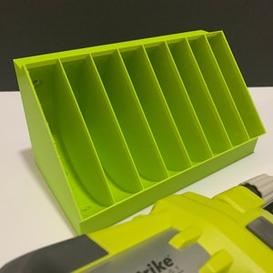 K&ouml;nnte beinhalten: Ein limegr&uuml;ner Plastik-Organizer mit sieben F&auml;chern zur Aufbewahrung von Kleinteilen. Der Organizer ist schr&auml;g gestellt und hat ein kleines Schraubenloch an der Seite. Ein limegr&uuml;nes Elektrowerkzeug ist im Vordergrund zu sehen.