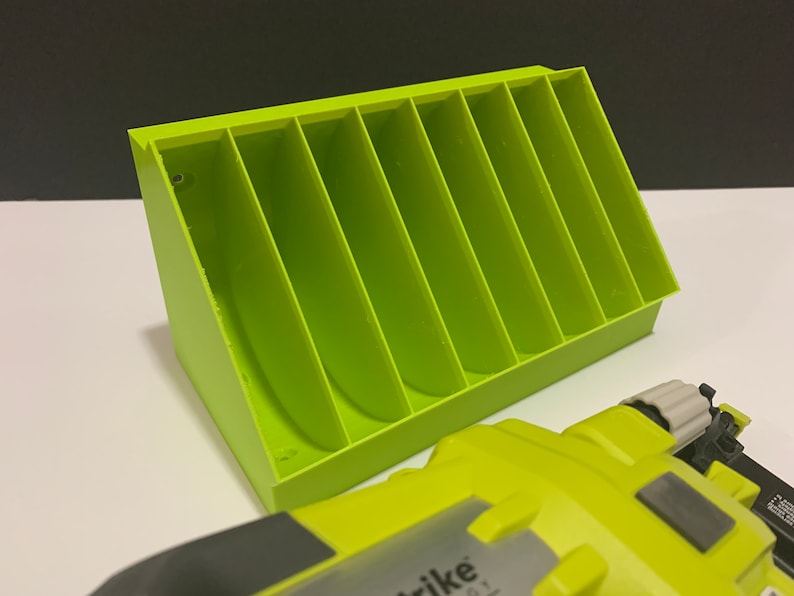 K&ouml;nnte beinhalten: Ein limegr&uuml;ner Plastik-Organizer mit sieben F&auml;chern zur Aufbewahrung von Kleinteilen. Der Organizer ist schr&auml;g gestellt und hat ein kleines Schraubenloch an der Seite. Ein limegr&uuml;nes Elektrowerkzeug ist im Vordergrund zu sehen.