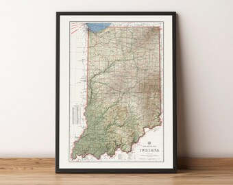 Op de afbeelding: Een vintage kaart van Indiana in een zwart frame. De kaart is gedrukt op wit papier en toont de topografie van de staat in groene en bruine kleuren. De kaart heeft de titel "State Road Map of Indiana".