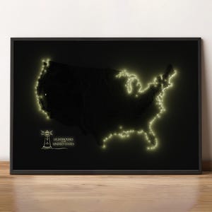 May include: A framed black print featuring a map of the United States with glowing outlines of the coastline. The image includes a lighthouse graphic and the text "Lighthouses United States". The print is displayed on a wooden surface.