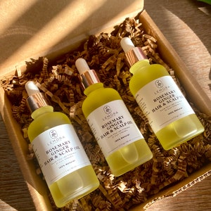 May include: Three amber glass bottles with gold droppers containing rosemary and ginger hair and scalp oil. The bottles are in a brown cardboard box with shredded paper packing. The labels on the bottles read "Lemora Rosemary Ginger Hair & Scalp Oil 100% Natural 1.7 fl oz / 50 ml".
