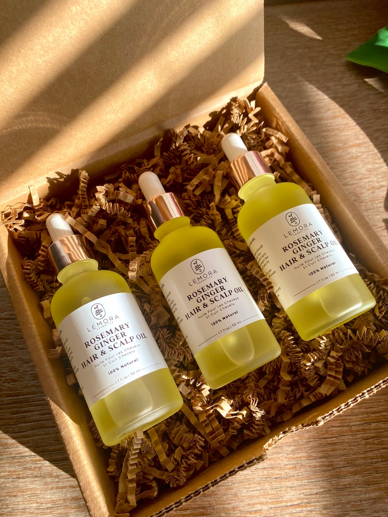 May include: Three amber glass bottles with gold droppers containing rosemary and ginger hair and scalp oil. The bottles are in a brown cardboard box with shredded paper packing. The labels on the bottles read "Lemora Rosemary Ginger Hair & Scalp Oil 100% Natural 1.7 fl oz / 50 ml".