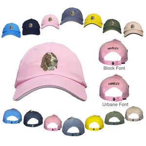 May include: A pink baseball cap with a white brim and a brown and white dog embroidered on the front. The cap is shown in different colors and with different text on the back, including "Marley" in a block font and "Marley" in a cursive font.