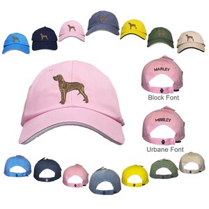 May include: A pink baseball cap with a brown and white dog embroidered on the front. The cap has a white brim and a white underside. The cap is shown in different colors, including blue, green, yellow, and beige. The cap also has a black font that says "MARLEY" on the back.