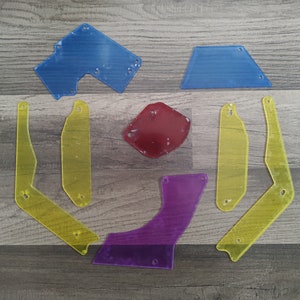 May include: A collection of colorful, transparent plastic shapes in blue, yellow, red, and purple. The shapes include a trapezoid, a curved piece, and several angular forms, all with small holes.
