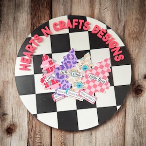 May include: A round decorative piece with a black and white checkered pattern. The words "HEARTS N CRAFTS DESIGNS" are in pink letters around the edge. Several tree-shaped cutouts with various patterns and the words "Little Trees" are on the surface.
