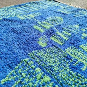 May include: A blue and green patterned rug with a fuzzy texture. The rug has a geometric design with a repeating pattern.