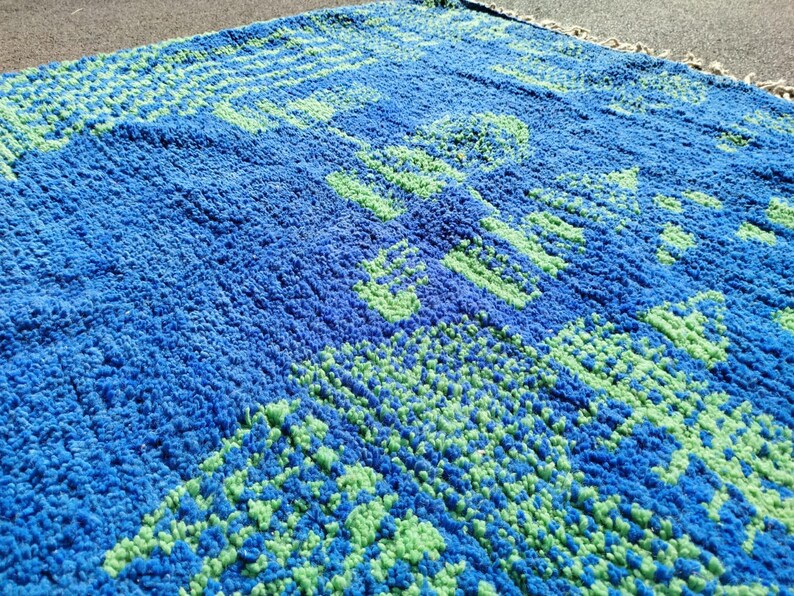 May include: A blue and green patterned rug with a fuzzy texture. The rug has a geometric design with a repeating pattern.