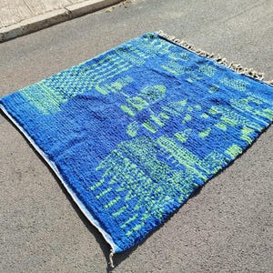 May include: A blue and green patterned rug with a fringed border. The rug features a geometric design with a variety of shapes and sizes.