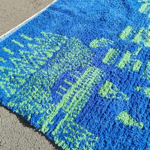 May include: Blue and green bath mat with a geometric pattern. The mat has a fluffy texture.